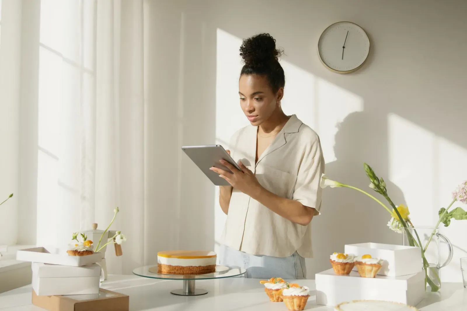 A bakery owner checking orders on a tablet in her bright shop